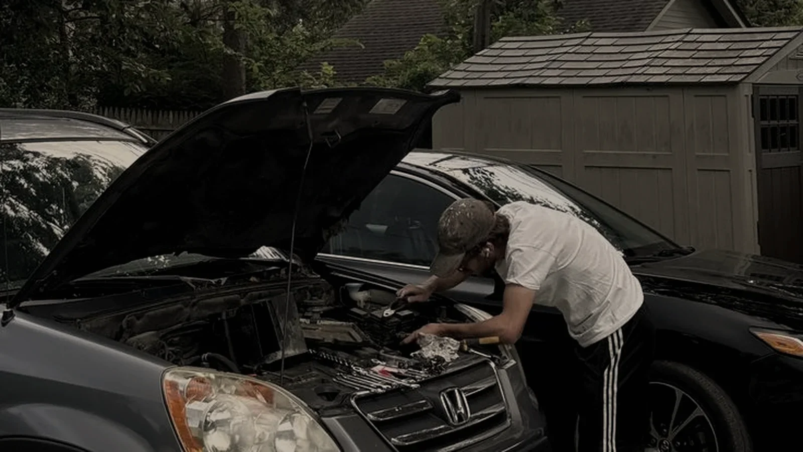 Car owner carrying out maintenance under the bonnet on a driveway.